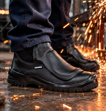Bota industrial negra con protección metatarsal especializada expuesta a chispas de soldadura en taller.