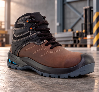 Bota de seguridad industrial de piel color café con suela robusta y refuerzo protector en entorno de almacén.