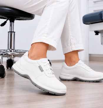 Persona sentada en un consultorio médico usando zapatos ocupacionales blancos con suela antiderrapante.